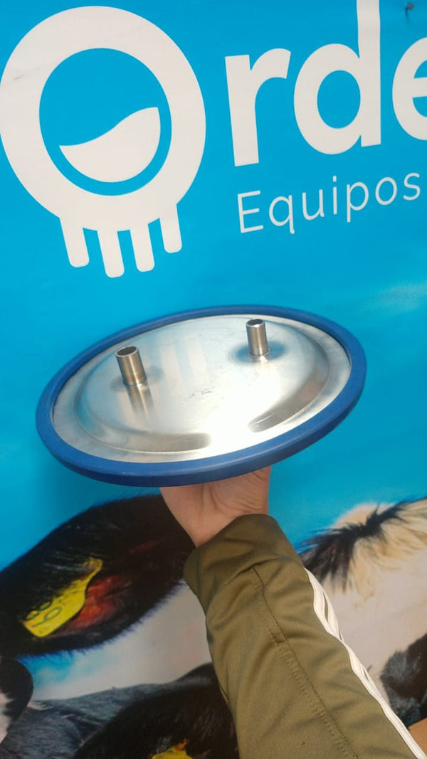 Tapa de ordeño a cantina en acero inoxidable con empaque azul, vista por debajo: en una de sus bocas se monta la trampa de seguridad — foto real