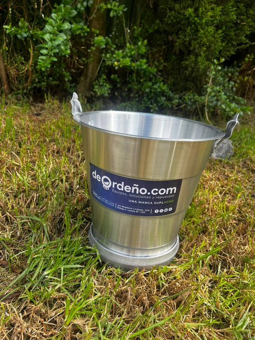 Balde lechero de 11 litros en aluminio, sobre el pasto de una finca, con el aro de refuerzo visible en la base
